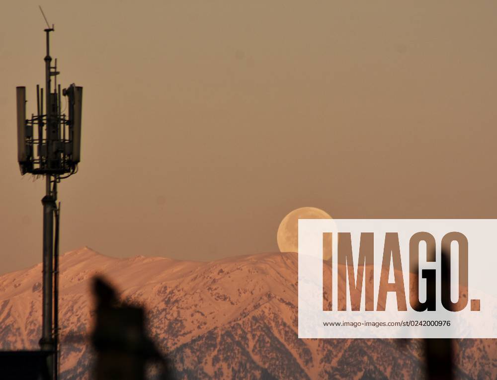 India: Pink Moon 2023 Full moon sets above Snow covered Himalayan range of mountains, Kashmir, the Summer captial of Indian Administrated Kashmir, on April 7, 2023. April full moon is also known as pink, egg and fish moon. Srinagar Jammu and Kashmir India Srinagar