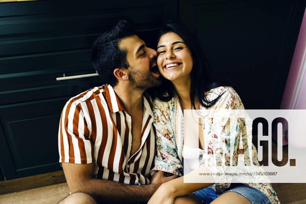 Romantic man biting cheek of happy girlfriend sitting at home model released, Symbolfoto property released, JJF00477