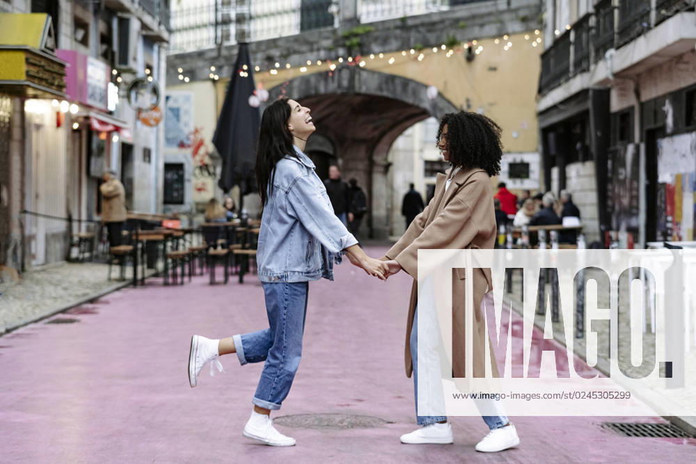 IMAGO Creative, Urban Lifestyle Cheerful friends holding hands and enjoying on footpath model released, Symbolfoto, JJF00594