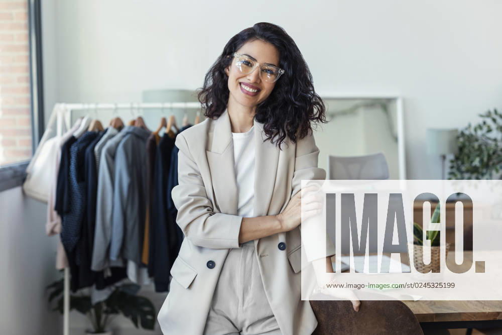 Happy fashion designer wearing eyeglasses leaning by desk in studio model released, Symbolfoto property released, JSRF02496