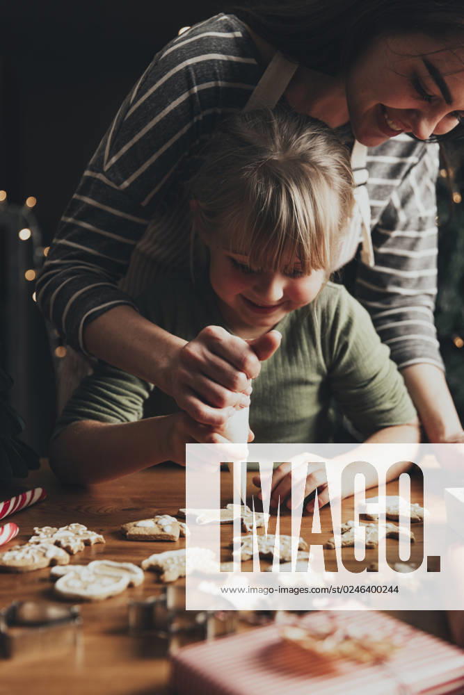 Christmas, New Year food preparation. Gingerbread cookies decorating with icing Christmas, New Year gingerbread cooking, making, decorating freshly baked cookies with icing and mastic. Mommy and child, authentic lovely moments. Mom helping cute little daughter to decorate cookie ,model released, Symbolfoto