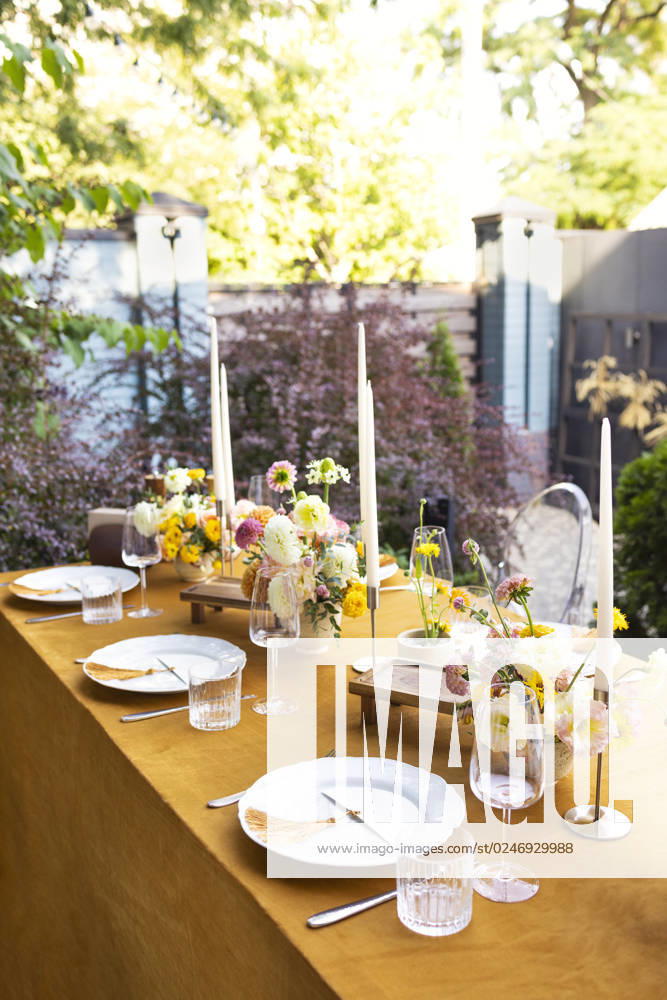 Wedding table for guests, decorated with candles, are served with cutlery and crockery and covered with yellow tablecloth Wedding. Banquet. Chairs and a table for guests, decorated with candles, are served with cutlery and crockery and covered with yellow tablecloth. The table stands on a green lawn in the backyard banquet area