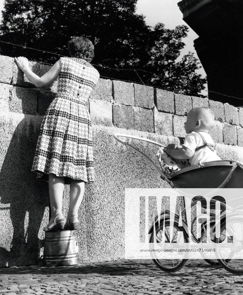 Eine junge Mutter schaut über die Mauer Eine junge Mutter, dahinter ihr Kind in seinem Kinderwagen, schaut über die Mauer in der Bernauer Strasse in den Ostsektor von Berlin, Deutschland 1961., Berlin