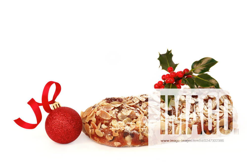 Stollen christmas cake with decorative holly leaf sprig and red berries with a sparkling red bauble, over white background.
