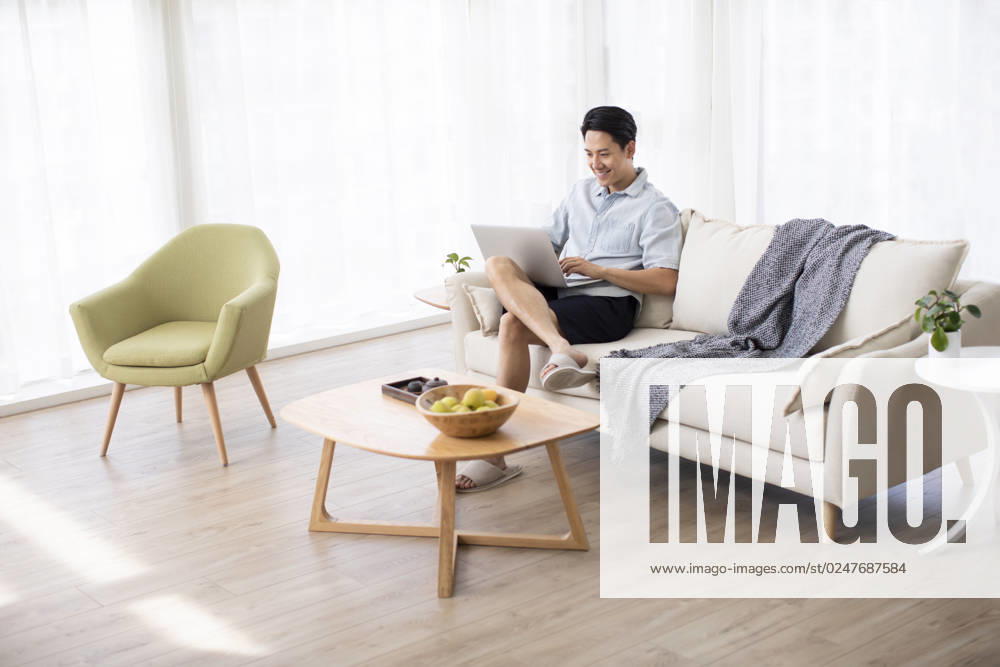 Happy young Chinese man using laptop in living room Beijing China