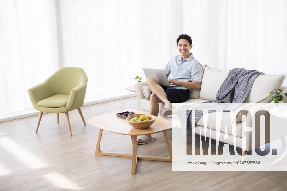 Happy young Chinese man using laptop in living room Beijing China