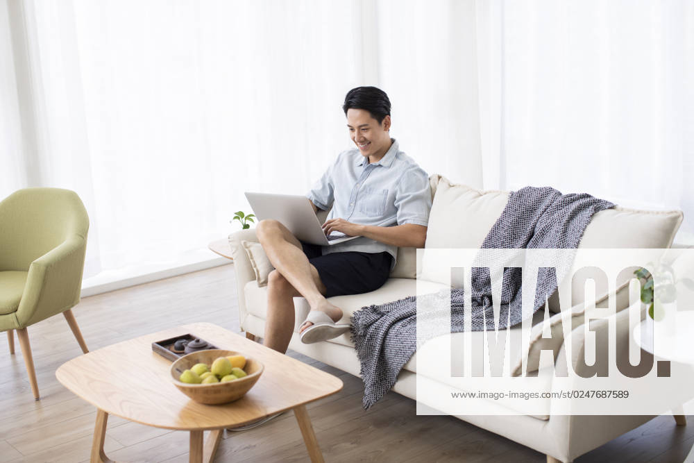 Happy young Chinese man using laptop in living room Beijing China
