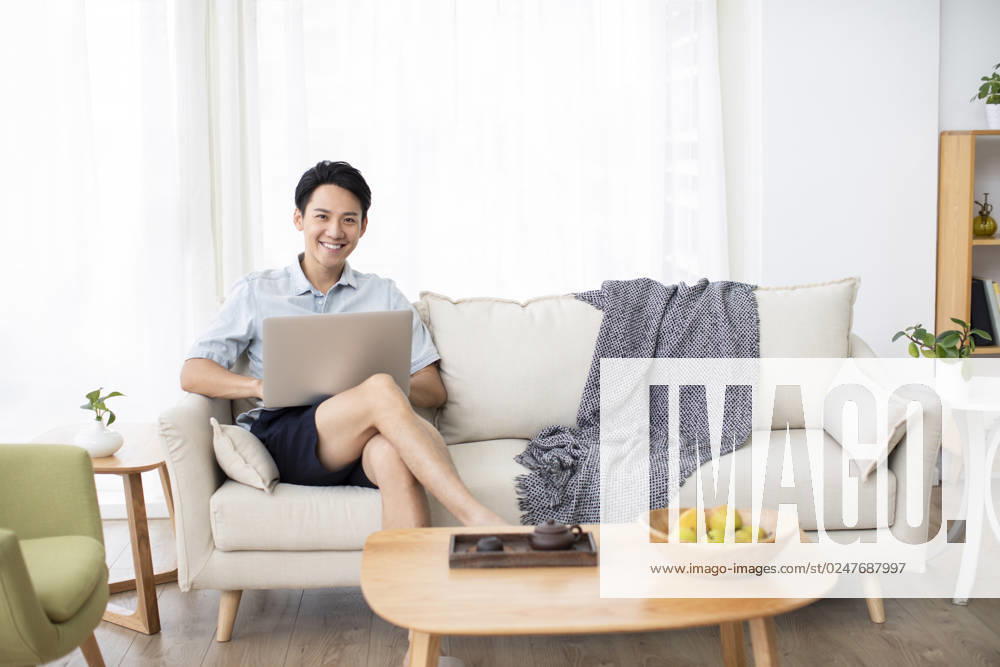 Happy young Chinese man using laptop in living room Beijing China
