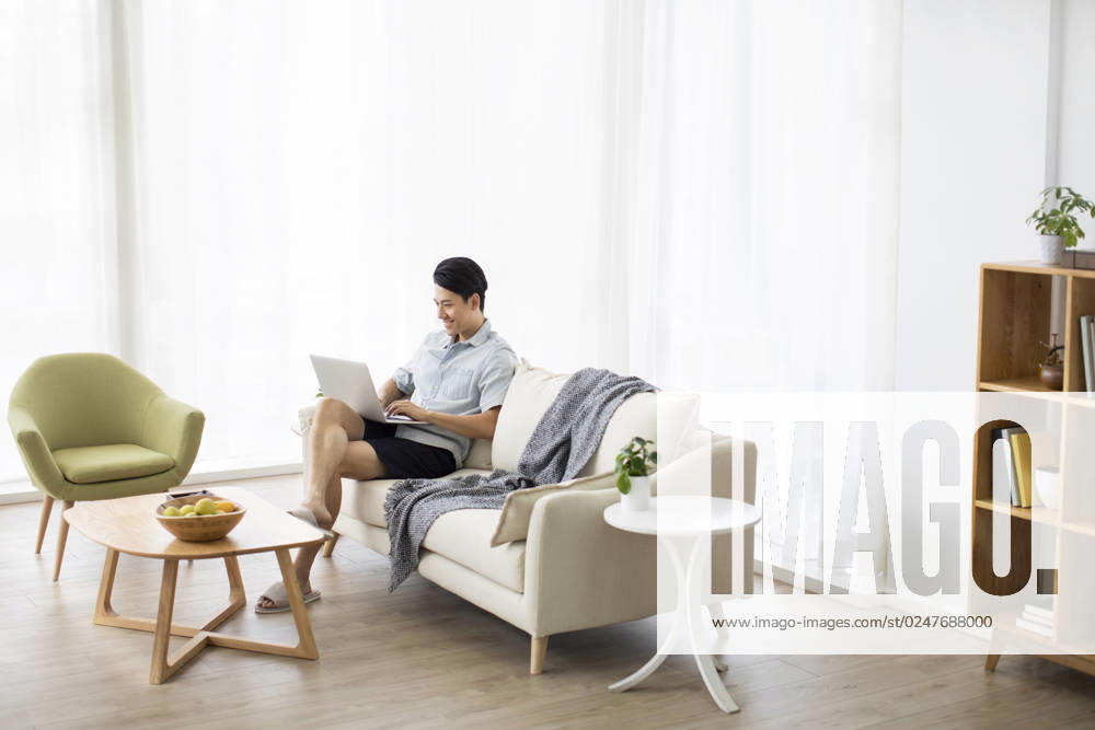 Happy young Chinese man using laptop in living room Beijing China