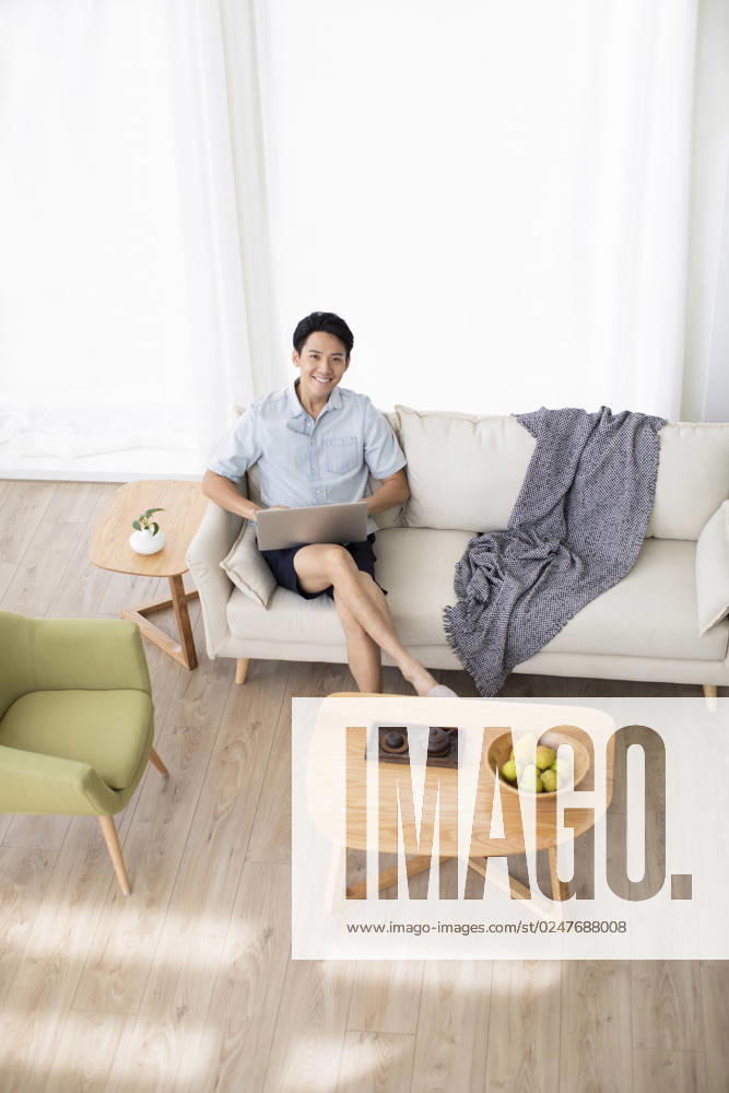 Happy young Chinese man using laptop in living room Beijing China