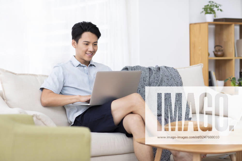 Happy young Chinese man using laptop in living room Beijing China