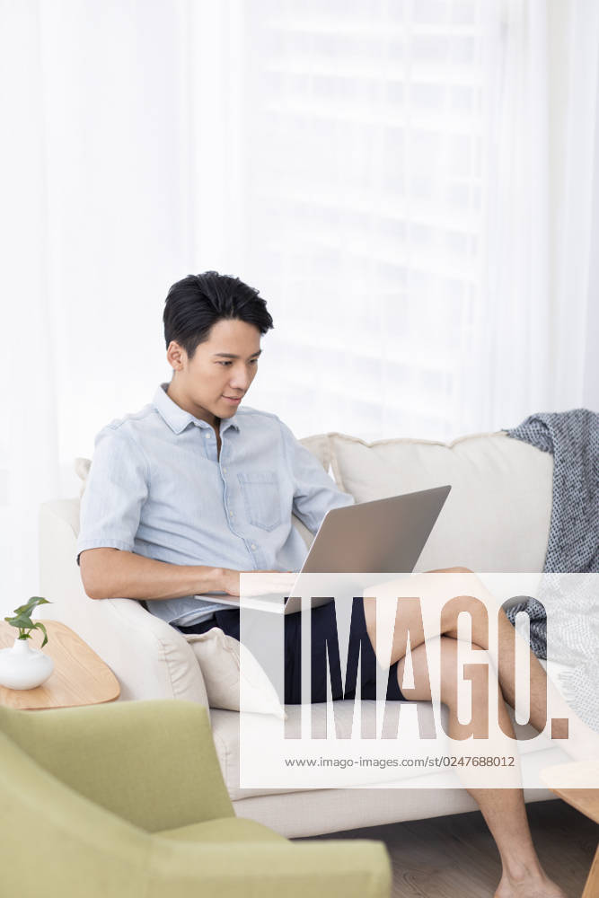 Happy young Chinese man using laptop in living room Beijing China