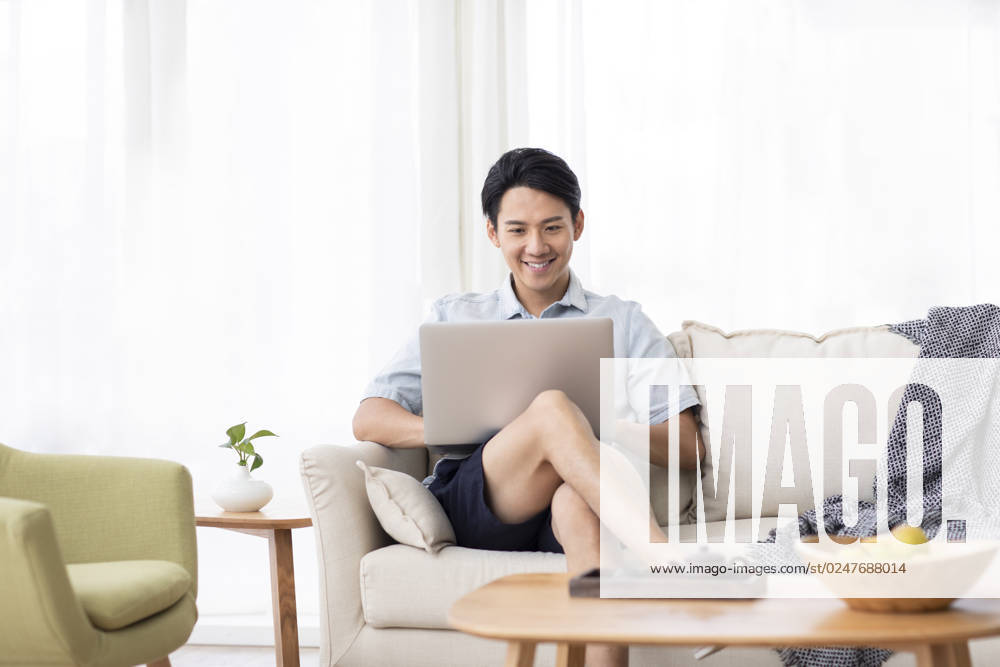 Happy young Chinese man using laptop in living room Beijing China