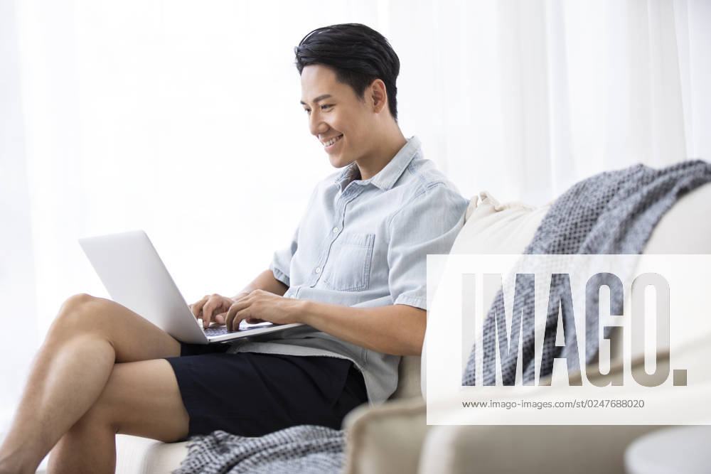 Happy young Chinese man using laptop in living room Beijing China