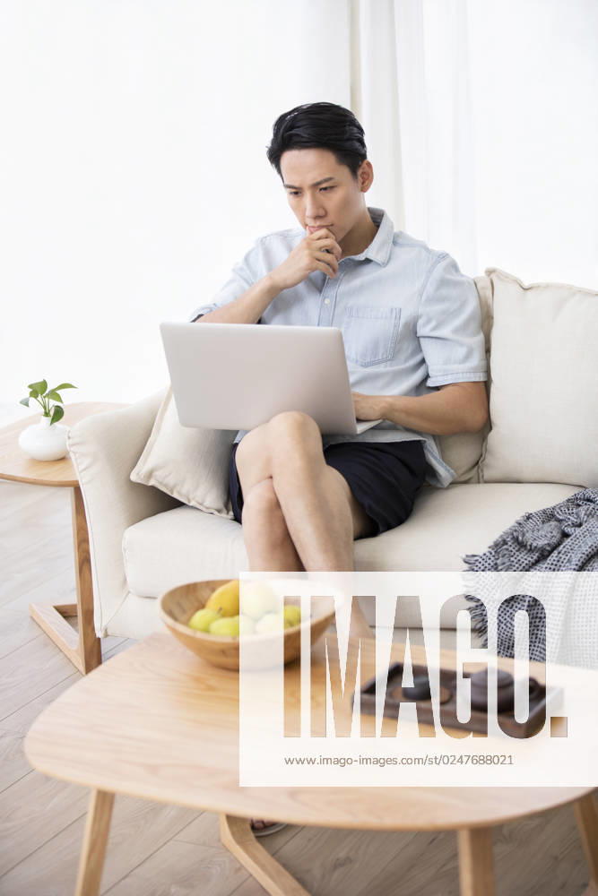 Happy young Chinese man using laptop in living room Beijing China