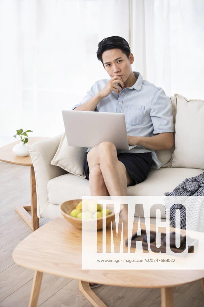 Happy young Chinese man using laptop in living room Beijing China