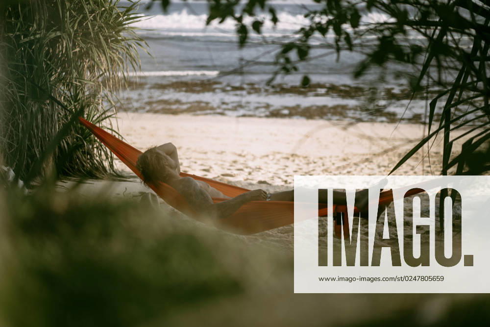 A young man rests and chills in an orange hammock on the beach n Nusa Penida, Bali, Indonesia CR_YUKI230221-1130713-01 ,model released, Symbolfoto ,property released