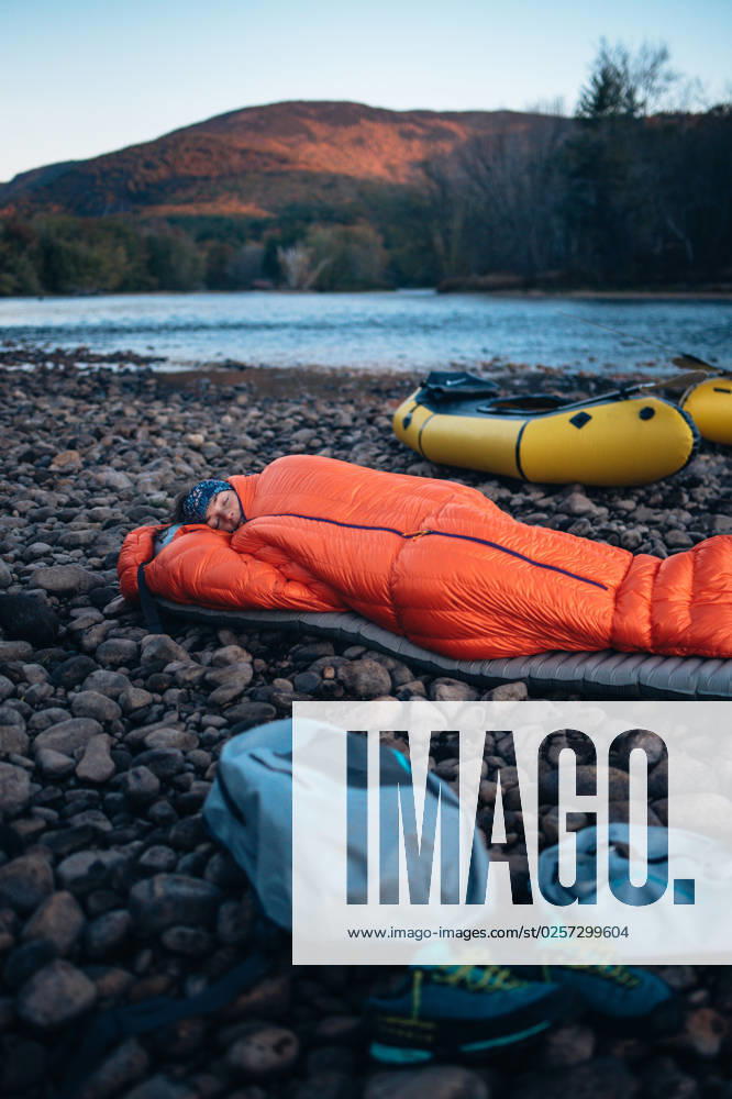 Woman asleep in sleeping bag on river edge with pack rafts Shelburne, New Hampshire, United States CR_BRDO2302087A-1123619-01 ,model released, Symbolfoto