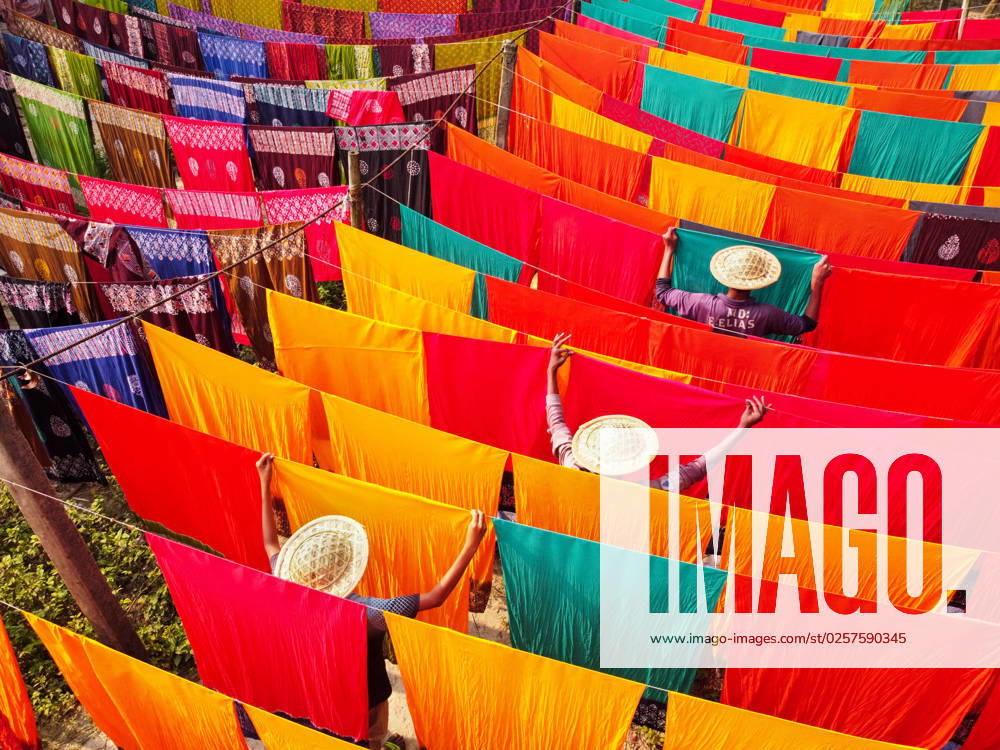 Workers hang hundreds of color-dyed sheets of cloth on a bamboo framework to dry in a dyeing factory in Narayanganj, Bangladesh. The drying process usually takes 4 hours, with each set of 200 pieces at a time to dry in temperatures over 42 degrees Celsius. Workers use hats for protection from the scorching heat because they have to constantly turn the colorful fabrics so that they dry perfectly in the sunlight. Narayanganj Bangladesh - ZUMAs231 20230523_zip_s231_015