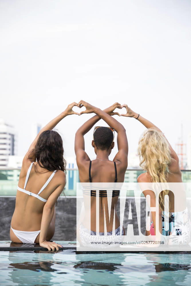 Friends making heart gesture sitting at poolside model released, Symbolfoto, IKF00441
