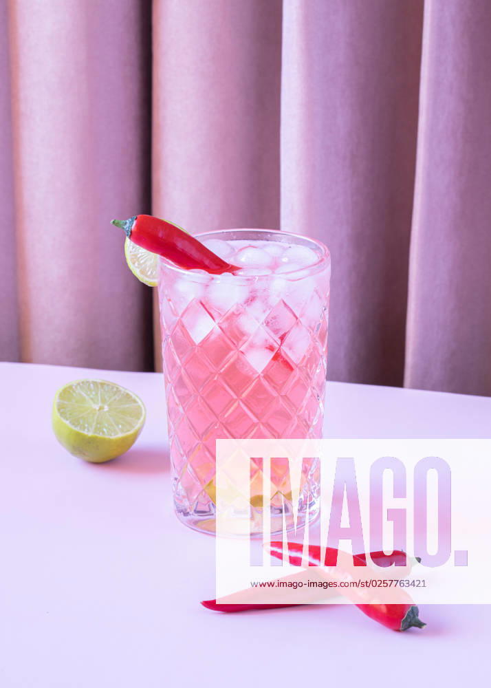 Clear glass filled with chilled refreshing cocktail served with pepper and ice cubes placed on the table with lime and peppers BegoSimon_ID13908_419616_004