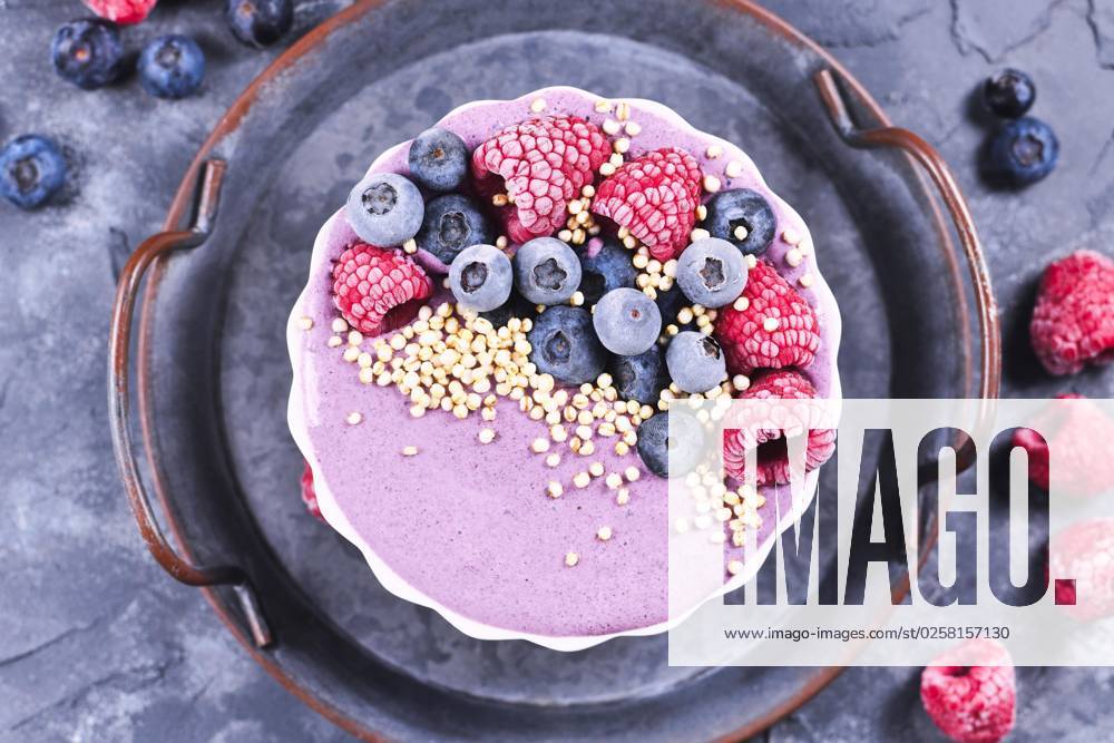 Fruit smoothie bowl with pink yogurt decorated with healthy raspberry, blueberry and puffed quinoa grain on iron tray