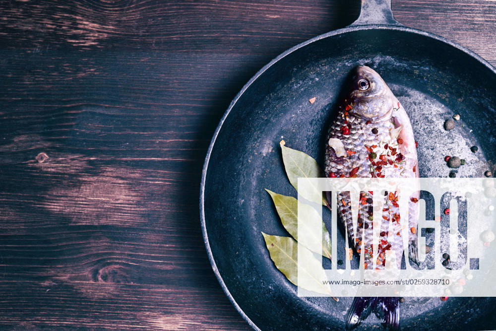 IMAGO Creative, Food, Karpfen-Saison Carp fish in a black cast-iron frying pan on a brown wooden background, empty space on the left , 30785950.jpg, crucian, closeup, table, pepper, paprika, natural, spice, kitchen, delicious, green, whole, brown, leaf, gourmet, top, wood, healthy, milled, above, cook, seasoning, ingredient, wooden, vintage, background, board, fresh, cooking, fish, nature, food, edible, raw, bay leaf, top view, plank, carp, empty space