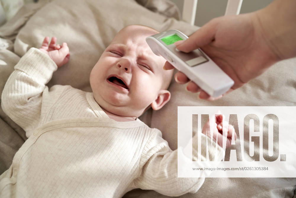 Mother checking temperature of crying baby lying in crib at home model released, Symbolfoto, ABIF01985