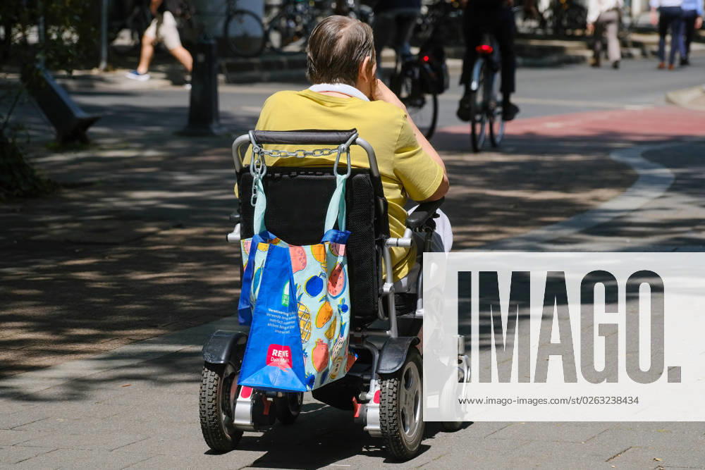 Dusseldorf 10 07 2023 Rewe shopping bag wheelchair wheelchair driver senior senior citizen old age infirmity frailty old age frailty care care need handicap disabled care insurance Dusseldorf North Rhine Westphalia Germany