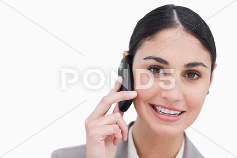 Close up of smiling businesswoman talking on cellphone against a white background 20s,Young Adult,Woman,Caucasian,Beautiful,Businesswoman,Career,Confident,Elegant,Employee,Happy,Pretty,Smile,Standing,Full Suit,Worker,Smiling,Well Dressed,Brown Hair,Tied Hair,Brunette,Mobile,Phone,Talking,Calling,Listening