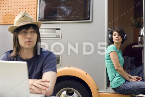 Germany, leipzig, ammelshainer see, young couple, man using laptop, woman listening to headphones hearing, vacation, people, caucasian appearance, leisure, communication, Wireless Technology, using, two people, adults, man, trailer, caravan, technical equipment, computer, laptop, Mobility, casual clothing, technology, dark hair, dark-haired, listening, music, relaxation, head phone, woman, Lifestyles, young adult, 20-30 years, 20-25 years, camping, headgear, girlfriend, hat, friend, couple, heterosexual couple, sitting, perspective, three quarter length, looking away, contemplation, straw hat, Connection, accessibility