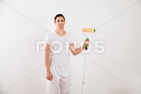 Portrait of smiling young man holding paint roller while standing against white wall at home adult, apartment, casual, caucasian, confidence, content, copyspace, cutout, decorator, development, diy, domestic, equipment, front, happiness, happy, holding, home, homeowner, house, housework, improvement, looking, maintenance, man, men, one, ownership, paint, painter, painters, painting, person, portrait, professional, redecoration, relocation, renovating, renovation, roller, rollers, smile, smiling, standing, view, wall, white, young