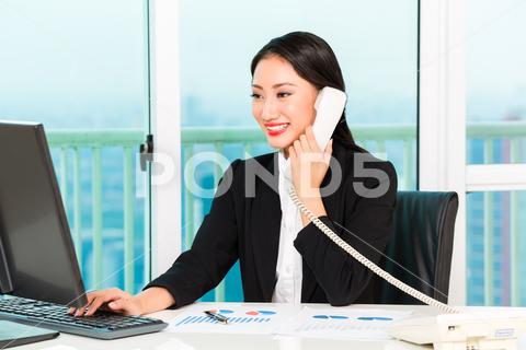 Close-up of smiling businesswoman talking on telephone looking at computer in the office woman, businesswoman, young, chinese, office, telephone, talking, using, keyboard, type, graph, report, communication, work, chair, workplace, desk, computer, technology, manager, executive, employees, portrait, closeup, business, corporate, professional, occupation, happy, smile, confident, natural, hand, hold, adult, one, people, person, waistup, formal, indoors, beautiful, smart, modern, lifestyle, attractive, front