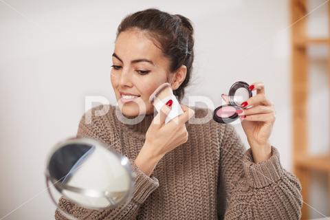 Portrait of smiling young woman applying powder and blush while doing make up at home, copy space {Smiling,Beauty,Holding,Cheerful,Beautiful,Happiness,Looking,Beauty Product,Close-up,Mirror,Applying,Casual Clothing,Fashion,Sitting,Portrait,Beautiful People,Cute,Clothing,Sweater,video,vlog,vlogging,influencer,following,social media,social,media,industry,review,like,subscribe,camera,recording,studio,guru,lifestyle,coach,makeup,make up,tutorial,cosmetics,beuty,young,woman,one,channel}