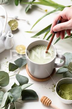 A vertical shot of Green tea latte with milk in a white cup with green leaves and wooden spoon tea, green, latte, drink, cup, beverage, food, hot, milk, white, coffee, background, cafe, sweet, table, cream, fresh, breakfast, refreshment, mug, healthy, matcha, japanese, green tea, glass, cappuccino, espresso, liquid, natural, chinese, foam, morning, wooden, wood, tasty, powder, brown, oriental, caffeine, cold, nutrition, relax, cool, iced, ice, organic, delicious, smoothie, nobody, isolated