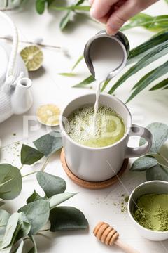 A vertical shot of Green tea latte with milk in a white cup with green leaves and wooden spoon tea, green, latte, drink, cup, beverage, food, hot, milk, white, coffee, background, cafe, sweet, table, cream, fresh, breakfast, refreshment, mug, healthy, matcha, japanese, green tea, glass, cappuccino, espresso, liquid, natural, chinese, foam, morning, wooden, wood, tasty, powder, brown, oriental, caffeine, cold, nutrition, relax, cool, iced, ice, organic, delicious, smoothie, nobody, isolated