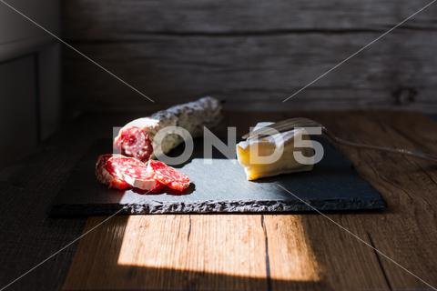A closeup shot of brie cheese and smoked sausages on a board snack, wooden, glass, white, gourmet, pork, food, background, smoked, closeup, drink, cold, fresh, meal, wood, table, studio, board, refreshment, slice, product, alcohol, cuisine, cheese, breakfast, party, meat, yellow, appetizer, tasty, sausage, beverage, bar, lager, froth, cut, ham, beer, liquid, ingredient