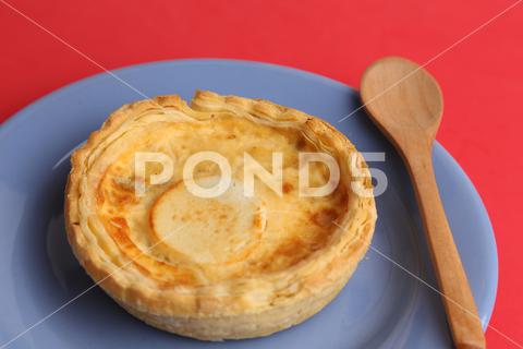 A closeup of delicious three cheese quiche next to a wooden spoon on a blue plate cheese, meal, snack, cooking, pie, dinner, plate, dish, food, appetizer, breakfast, parmesan, dairy, homemade, delicious, table, french, baked, gourmet, cream, dishware, lunch, cookery, rustic, traditional, fatty, pastry, products, tart, crust, crispy, closeup, bread, ingredient, quiche, wood, wooden, spoon