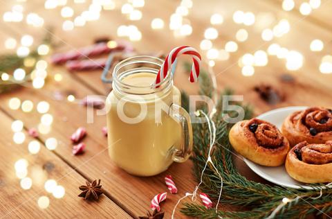 Christmas and seasonal drinks concept - eggnog in glass mug with candy cane decoration, cinnamon buns, fir tree brunch and garland lights on wooden background eggnog, christmas, drink, glass, mug, holiday, cocktail, alcohol, beverage, bun, cinnamon, candy cane, fir, branch, egg, liqueur, celebration, mason jar, traditional, seasonal, x-mas, xmas, ingredient, sweet, treat, pastry, bake, anise, sugar, star anise, brown, cup, new year, lights, garland, spice, festive, decoration, candy, homemade, flavor, still life, nobody, object, concept, hygge, wooden, board