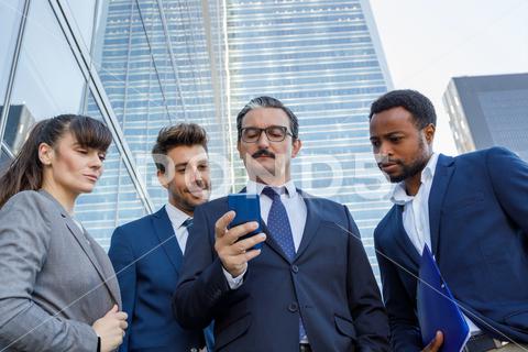 Group of happy multiracial colleagues in classic suites laughing while reading good news on smartphone standing together on street people, laugh, read, smartphone, good news, happy, style, together, spend time, having fun, street, cheerful, group, multiracial, multiethnic, diverse, discuss, classic, gadget, device, joy, colleague, using, browsing, share, mobile, phone, chat, businesspeople, job, business, entrepreneur, excited, message, optimist, friendship, delight, employee, cooperate, coworker, social media, sunlight, partner, startup, manager, workplace, building, lifestyle, outdoors, blurred background