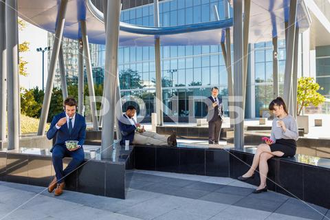 Group of young multiracial coworkers in classy outfits sitting on bench near modern business center and having lunch people, lunch, coffee break, rest, bench, together, business, skyscraper, city, relax, coworker, modern, group, multiracial, multiethnic, diverse, young, classy, eat, using, smartphone, drink, exterior, glass wall, reflection, sunlight, recreation, professional, employee, team, style, colleague, contemporary, listen, music, headphones, coffee, trendy, leisure, food, takeaway, enjoy, meal, company, street, chill, staff, lifestyle, outdoors, blur