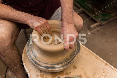 Crop unrecognizable sculptor with equipment giving shape while sculpting with brown clay on throwing wheel man, shape, clay, sculpt, equipment, process, motion, jug, ceramic, skill, male, sculptor, workshop, art, artist, handicraft, earthenware, ceramist, craft, create, dirty, form, hobby, handmade, maker, master, molding, occupation, pottery, utensil, wet, wheel, professional, work, artisan, throw, small business, talent, workplace, crop, unrecognizable, faceless, anonymous, horizontal, body part, blur, indoors, top view, from above