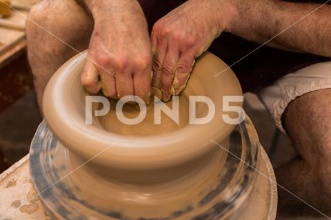 Crop unrecognizable sculptor with equipment giving shape while sculpting with brown clay on throwing wheel man, shape, clay, sculpt, equipment, process, motion, jug, ceramic, skill, male, sculptor, workshop, art, artist, handicraft, earthenware, ceramist, craft, create, dirty, form, hobby, handmade, maker, master, molding, occupation, pottery, utensil, wet, wheel, professional, work, artisan, throw, small business, talent, workplace, crop, unrecognizable, faceless, anonymous, horizontal, body part, blur, indoors, top view, from above