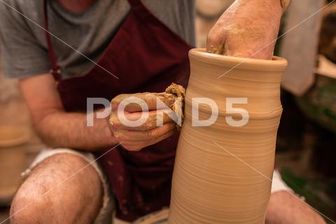 Crop unrecognizable sculptor with equipment giving shape while sculpting with brown clay on throwing wheel man, shape, clay, sculpt, equipment, process, motion, jug, ceramic, skill, male, sculptor, workshop, art, artist, handicraft, earthenware, ceramist, craft, create, dirty, form, hobby, handmade, maker, master, molding, occupation, pottery, utensil, wet, wheel, professional, work, artisan, throw, small business, talent, workplace, crop, unrecognizable, faceless, anonymous, horizontal, body part, blur, indoors