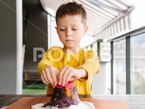 Concentrated little boy in casual clothes standing at table and molding plasticine while creating volcano figurine in workshop {{child,mold,plasticine,volcano,sculpt,creative,concentrate,boy,skill,craft,clay,create,sculpture,focus,childhood,molding,figurine,art,hobby,handwork,imagination,process,activity,workshop,figure,daytime,kid,interest,education,dough,colorful,casual,inspiration,talent,studio,decoration,handmade,adorable,manual,artwork,lifestyle,indoors,blurred background,horizontal}}