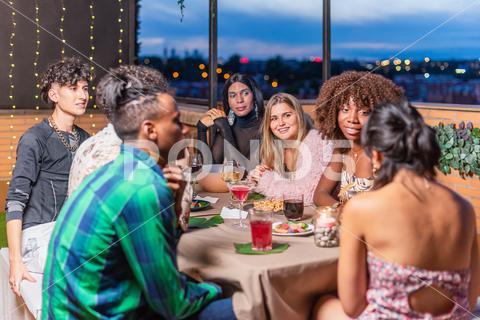 A group of friends celebrating New Year's Eve on the balcony of the house of one of them. caucasian, blonde, woman, asian, lifestyle, friends, sitting, togetherness, fun, drinking, cheerful, celebration, adult, talking, cocktail, group, happy, fashion, african american, horizontal, multi ethnic, happiness, friendship, enjoyment, multiracial group, terrace, balcony, 20s, people, young, smiling, diversity, party, eve, christmas, holiday, year, light, new year, home, xmas, indoors, joy, event, luxury, festive, evening, drink