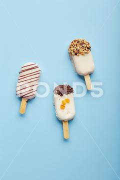Mousse dessert with fruit flavors in the form of popsicle ice cream covered with white chocolate on blue background. ice cream, sweet, mousse, dessert, delicious, food, cream, popsicle, homemade, lollipop, cold, sugar, stick, pastry, party, pop, shape, vanilla, tasty, sprinkle, fruit, glac, inside, flake, variety, copy, cupcake, filling, space, stacked, assortment, bright, cheesecake, nobody, closeup, cookie, fresh, plate, cool, chocolate, decoration, cake, gastronomy, meal