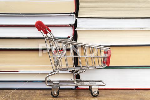 An empty shopping cart stands against the background of books. The concept of buying books in a bookstore or online. book,basket,shopping,business,school,concept,education,sale,marketing,supermarket,old,magazine,library,learning,store,retail,online,market,e-commerce,commerce,product,ideas,hardcover,wisdom,variety,trolley,bookstore,collection,selective,bookshop,buy,shopping- cart,consumerism,nobody,group,textbook,read,bookshelf,buyer,literary,literature,sell,purchase