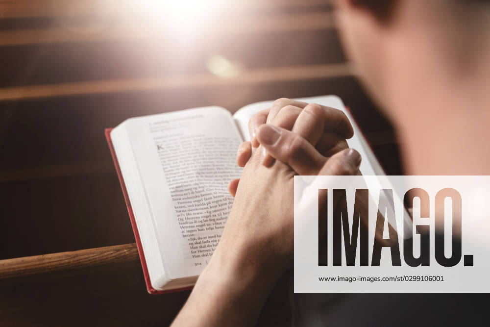 Young man praying to God in church with a Bible and folded hands. Faith in religion and faith in God concept. Praying in a church