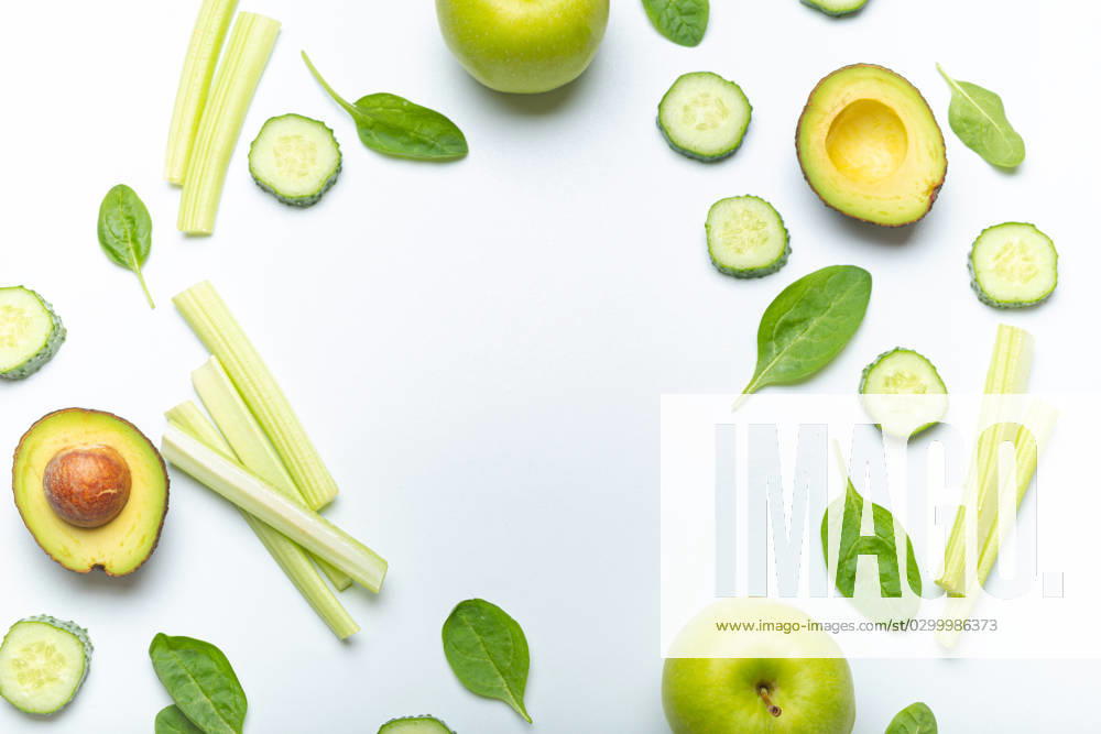 Bottle of green smoothie surrounded by green fruit and vegetables: apples, avocado, spinach, celery sticks, cucumber on white simple background top view. Diet, healthy nutrition, detox Bottle of green smoothie surrounded by green fruit and vegetables: apples, avocado, spinach, celery sticks, cucumber on white simple background top view. Diet, healthy nutrition, detox concept